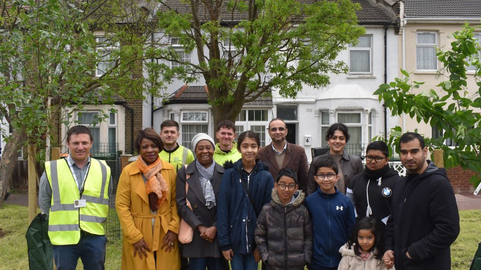 Children and adults stand in front of a tree