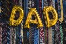 Golden balloons spell out the word dad in front of a wall of ties