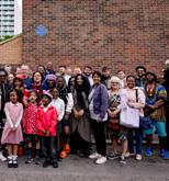 A group of people stand beneath a blue plaque 