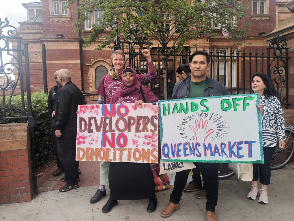 some people stand holding placards reading hands off Queen's Market