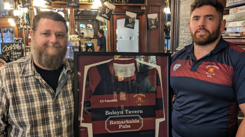 Two people in a pub pose next to a rugby shirt