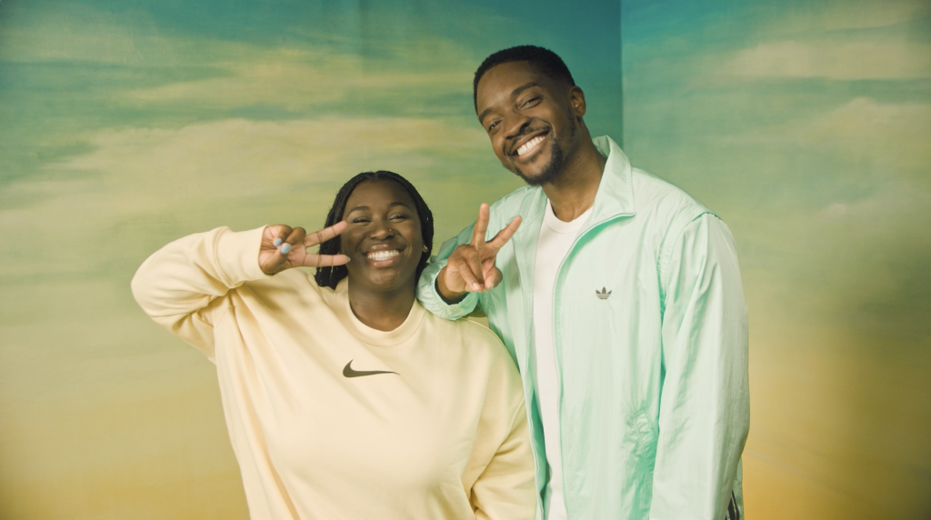 Two people hold their fingers in peace signs smiling at the camera