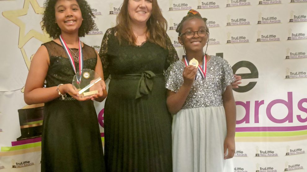 Two young people stand holding awards and medals
