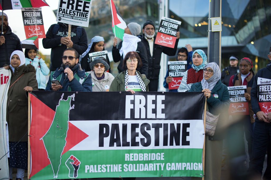 People stand with placards behind a banner which reads 'Free Palestine'