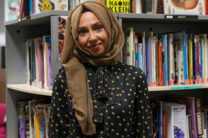 A person poses in from of shelves of books