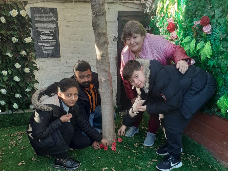 Children and adults surround a tree, placing poppies by its base.