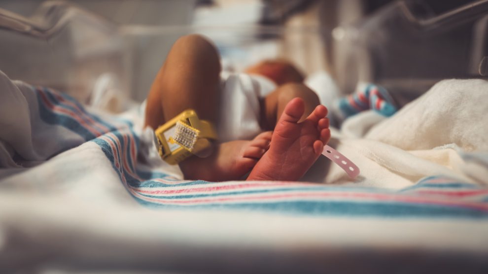 Baby lying in cot in hospital with tag on its right foot.