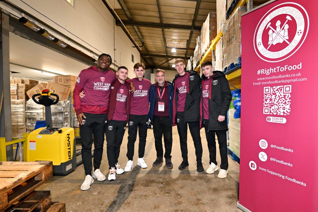 Young men in sports kit stand next to a large sign reading 'Irons Supporting foodbanks'