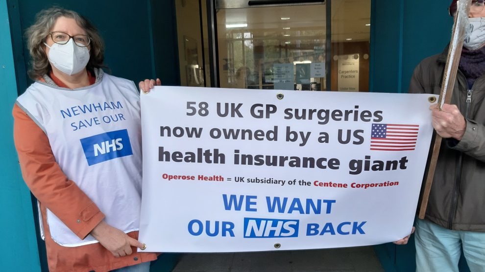Campaigners hold up a banner saying '58 UK Gp surgeries now owned by a US health insurance giant - We want our NHS back'