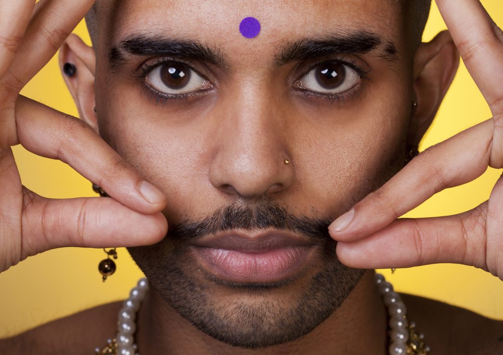 A portrait of a person, finger tips at moustache tip