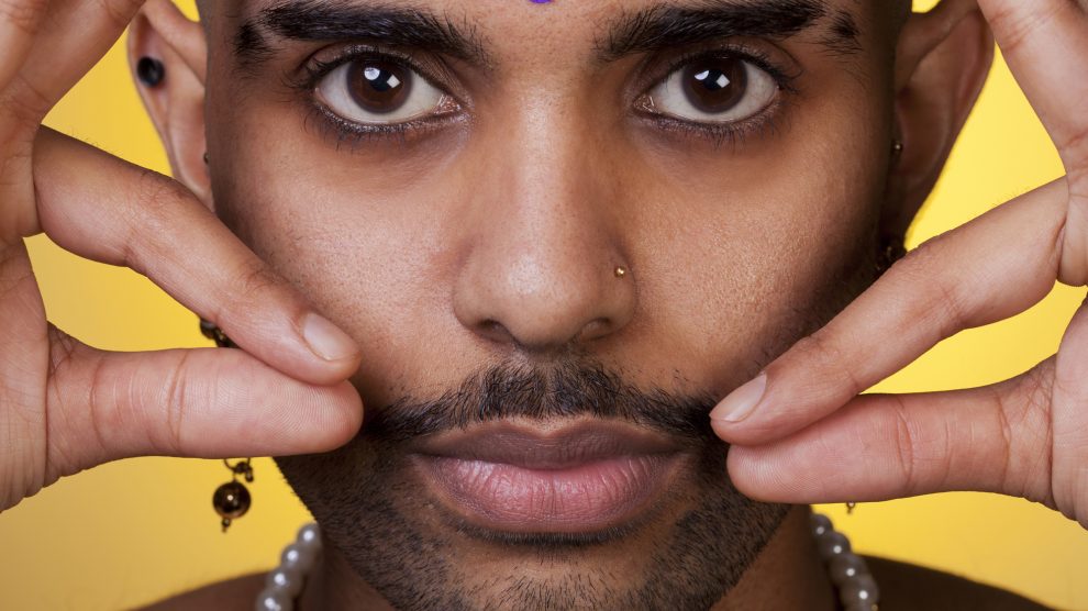 A portrait of a person, finger tips at moustache tip