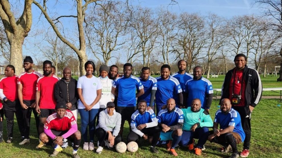A group of people pose with footballs in a park