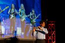 a person performs on a flute in front of a projection of people playing electric guitars