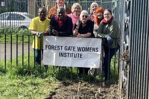 A group of women stand behind a banner reading Forest Gate Women's Institute with newly planted saplings in the foreground