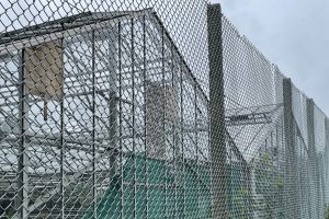An image of derelict greenhouses behind chain link fence