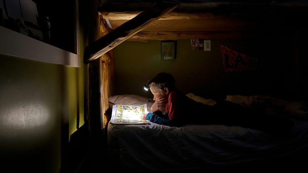 a child in a bunk reads by torchlight