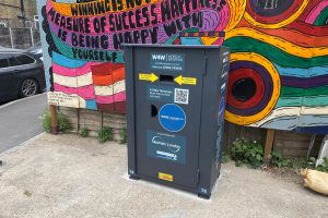 A metal knife amnesty bin in front of a brightly coloured mural