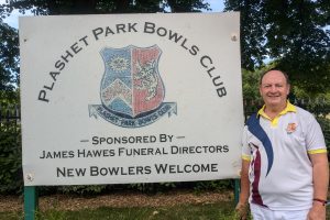a person stands by the sign advertising Plashet Park Bowls Club