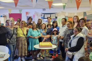 People under bunting stand around a celebratory cake