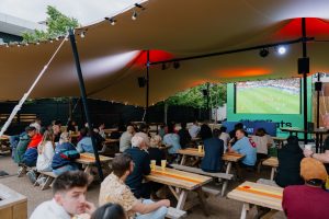 Excited punters watch sports on an open air big screen