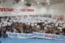 People in a sportshall hold a banner saying 'show your support #saveelgc'