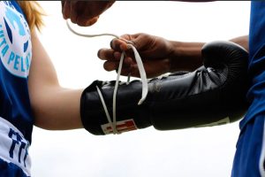 a person laces up boxing gloves for a young pugilist