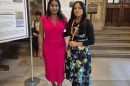 Two women in parliament standing in front of a noticeboard