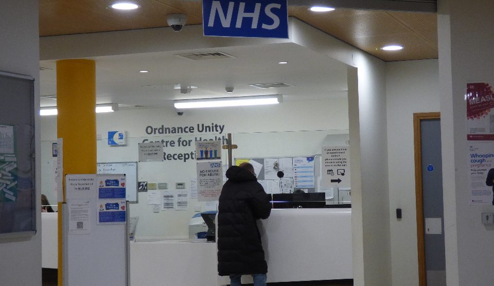 A woman at a counter with an NHS logo above it
