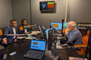 Two men with microphones talking to another men with a microphone in a radio studio