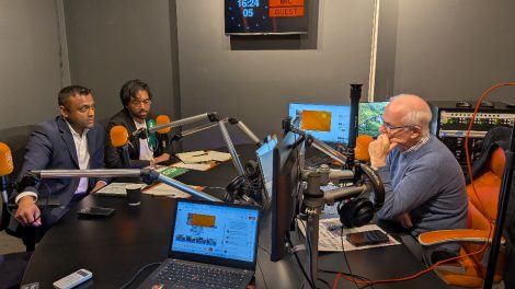Two men with microphones talking to another men with a microphone in a radio studio