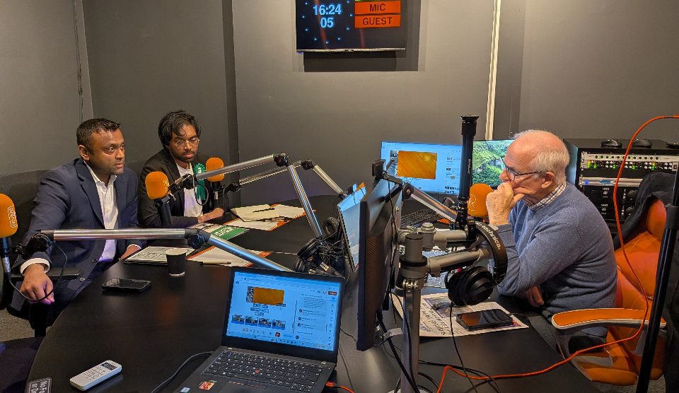 Two men with microphones talking to another men with a microphone in a radio studio